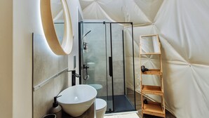 Un bagno moderno con cabina doccia in vetro, lavandino bianco e ripiano in legno.