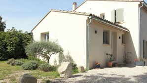 Un edificio a un piano con facciata beige, tetto in tegole e vialetto in ghiaia. In primo piano, vasi con piante e un grande masso.