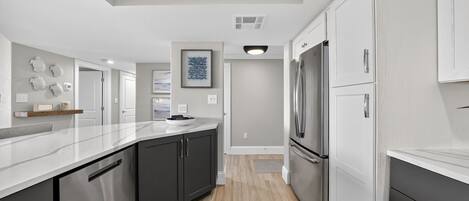 A modern kitchen with dark cabinets, stainless steel appliances, and a marble countertop.