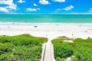 A beach with a wooden walkway leading to the water, surrounded by green vegetation. - Sundial L204 – 3 Bedroom Beachfront Luxury (Sanibel)