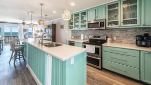 A modern kitchen with teal cabinetry, stainless steel appliances, and pendant lighting. - Gulf View Condo | Serene Escape with Heated Pool & Hot Tub (Corpus Christi)