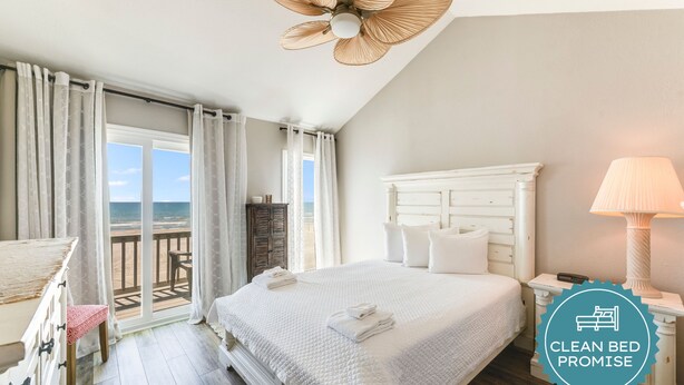 A clean, well-lit bedroom with a large bed, a nightstand, a lamp, and a view of the beach. - Gulf View Condo | Serene Escape with Heated Pool & Hot Tub (Corpus Christi)