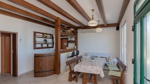 A dining area with wooden furniture, a table with a floral tablecloth, and a built-in shelf with glassware.