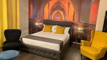 Habitación de hotel con una cama grande, dos sillones, una mesa redonda pequeña y un mural en la pared.
