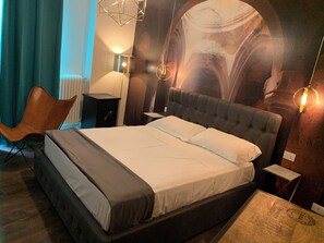 A bedroom with a large bed, a chair, a desk, and a wall with a mural. - Suite Lame 37 Rental Rooms (Bologna)