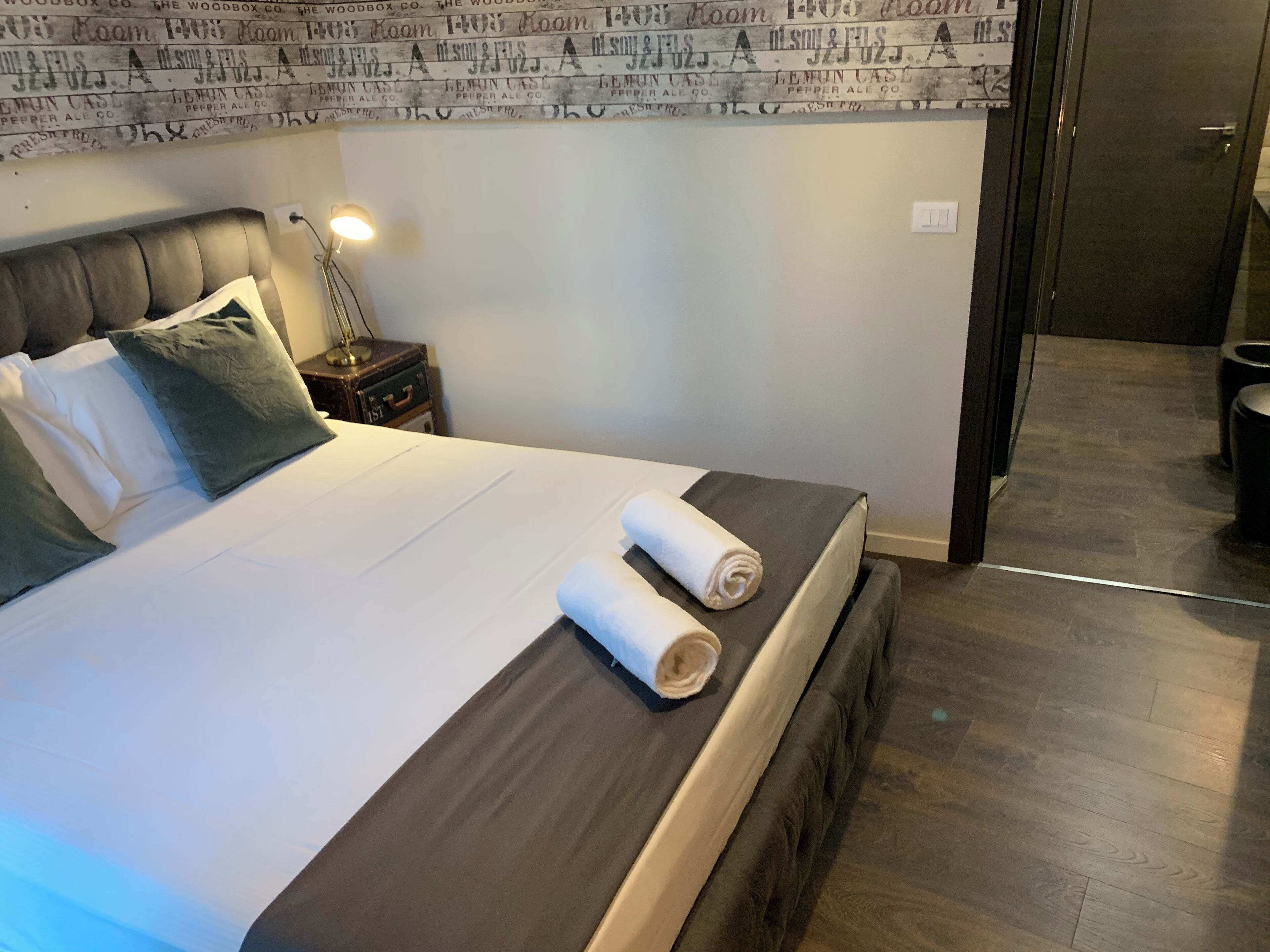 A hotel room with a bed, pillows, a nightstand, and a lamp.