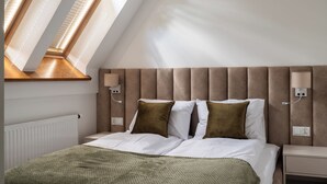 A bedroom with a sloped ceiling, a bed with white linens, two brown pillows, a green throw blanket, and a nightstand with a lamp. - Apartament przy Potoku 25 z parkingiem (Zakopane)