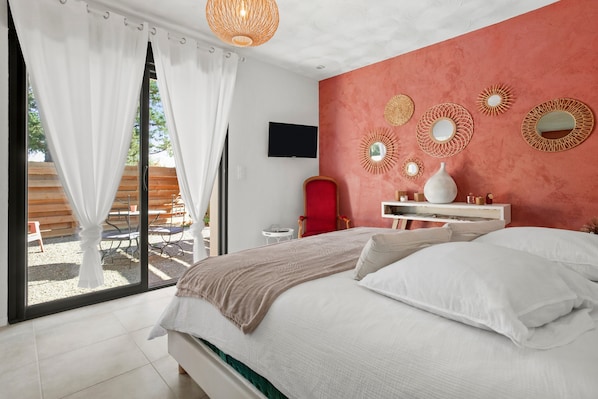 A bedroom with a bed, a TV, a red chair, and a wall with decorative mirrors.