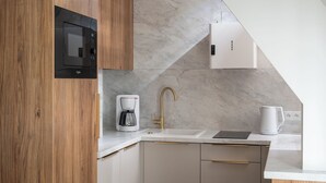 A modern kitchen with a built-in microwave, a coffee maker, a sink with a gold faucet, and a white kettle. - Apartament przy Potoku 26 z parkingiem (Zakopane)