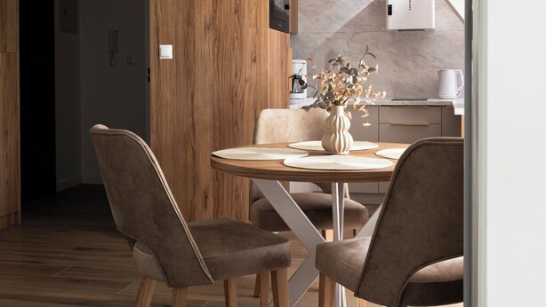 A modern kitchen with wooden cabinets, a marble countertop, and a dining area with a wooden table and chairs. - Apartament przy Potoku 26 z parkingiem (Zakopane)