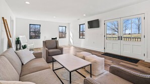 A spacious living room with a sectional sofa, a coffee table, and a gray armchair. There are large windows and a door leading to an outdoor area. - Modern Farmhouse Getaway (Leesburg)