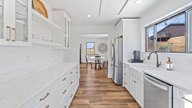 A modern kitchen with white cabinetry, a wooden floor, a dining area with a round table and chairs, and a view of a house through large windows. - Modern Farmhouse Getaway (Leesburg)