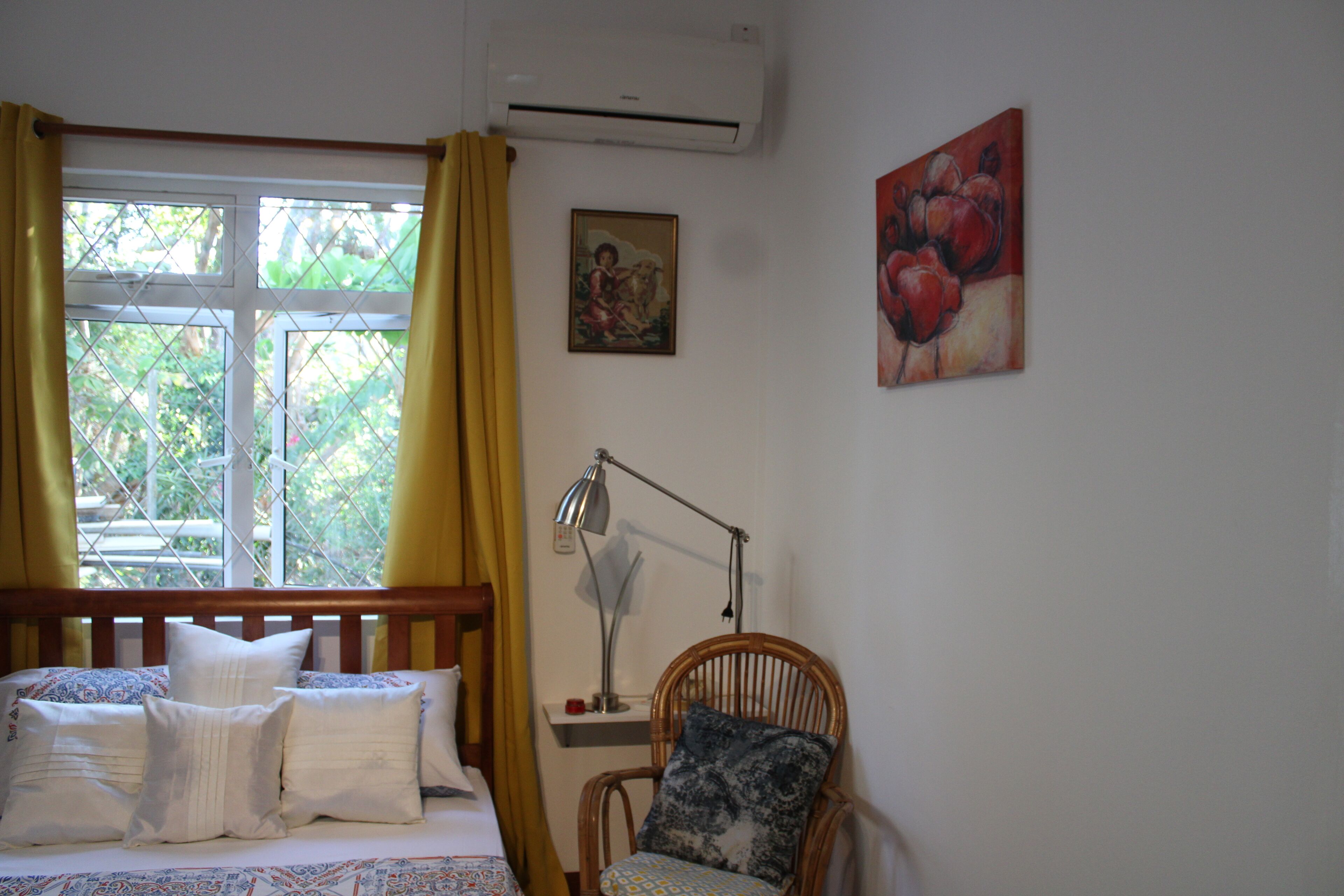Een slaapkamer met een bed, een stoel, een bureau met lamp en een raam met gordijnen.