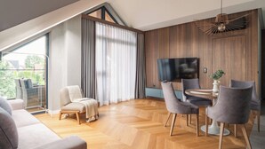 A modern living room with a herringbone wood floor, a large TV, and a dining area with grey chairs. - Apartament MONTE z jacuzzi i sauną (Zakopane)