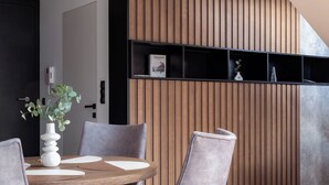 A modern dining area with a wooden table, grey upholstered chairs, and a hanging light fixture. - Apartament MONTE z jacuzzi i sauną (Zakopane)