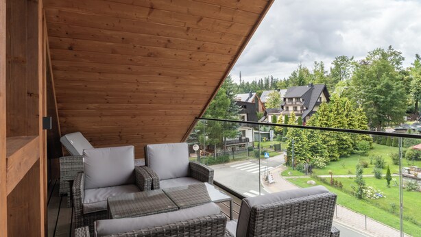 A balcony with wicker furniture and a view of a residential area. - Apartament MONTE z jacuzzi i sauną (Zakopane)