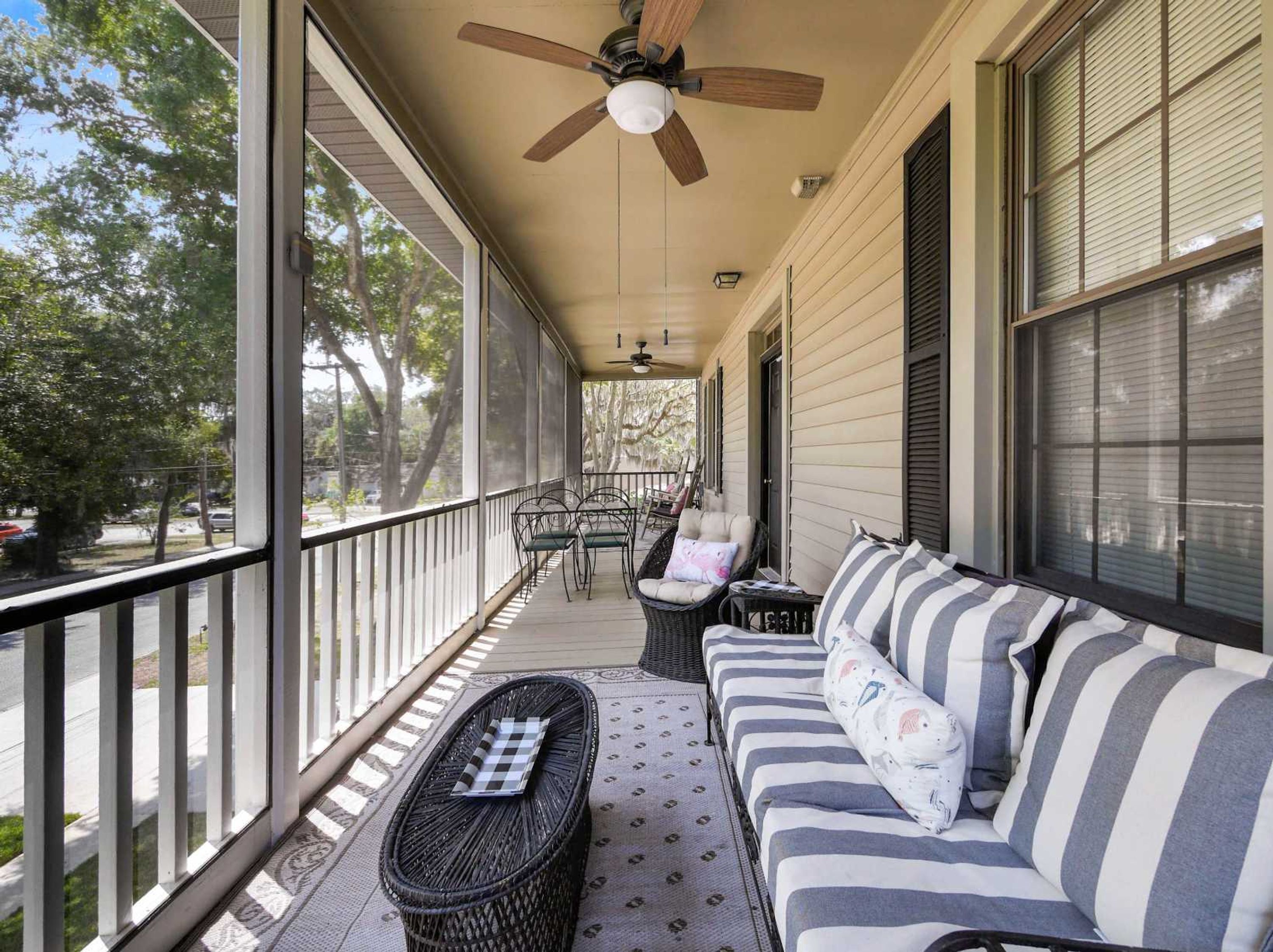 A covered porch with a ceiling fan, a striped sofa, a wicker table, and chairs.