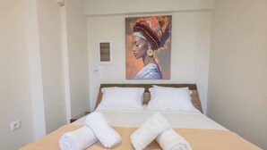 Una habitación de hotel con una cama bien hecha, dos toallas blancas enrolladas, un cuadro en la pared y una mesita de noche con una lámpara.