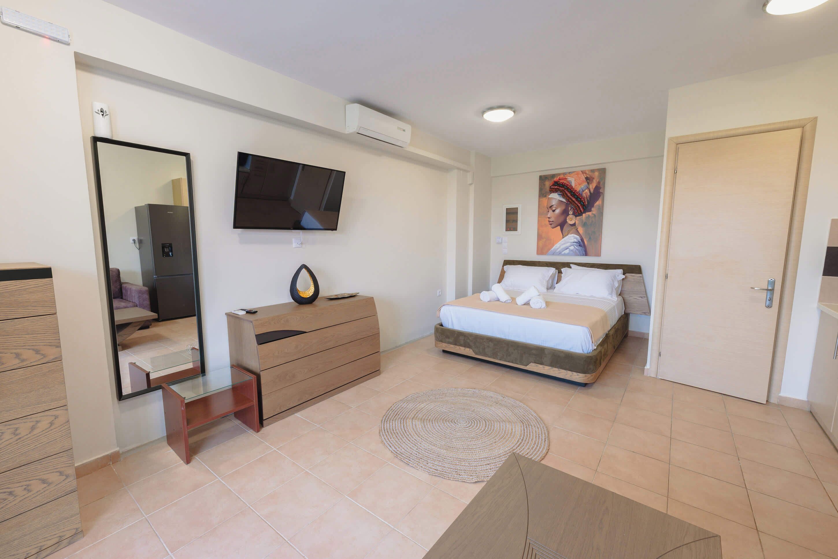 A modern bedroom with a bed, a dresser, a mirror, a flat-screen TV, and a painting on the wall.