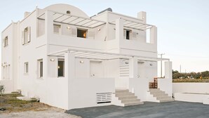 A modern two-story white building with a flat roof, a covered outdoor seating area, and a staircase leading to the upper floor.
