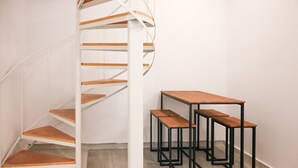 A spiral staircase with wooden steps and a white railing, adjacent to a set of three black metal tables with wooden benches.
