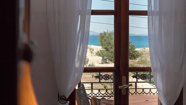 Uitzicht vanuit een kamer met een groot raam, uitkijkend op een strand met een heldere lucht.