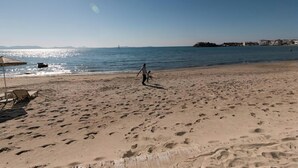 Een zandstrand met voetafdrukken, een heldere lucht en een zeilboot in de verte.