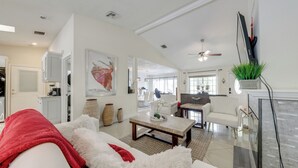 A spacious living room with a white sofa, a coffee table, and a fireplace. There is a kitchen area in the background with cabinets and a dining table. - Fishing Dock & Canal Views: Fort Lauderdale Home! (Fort Lauderdale)
