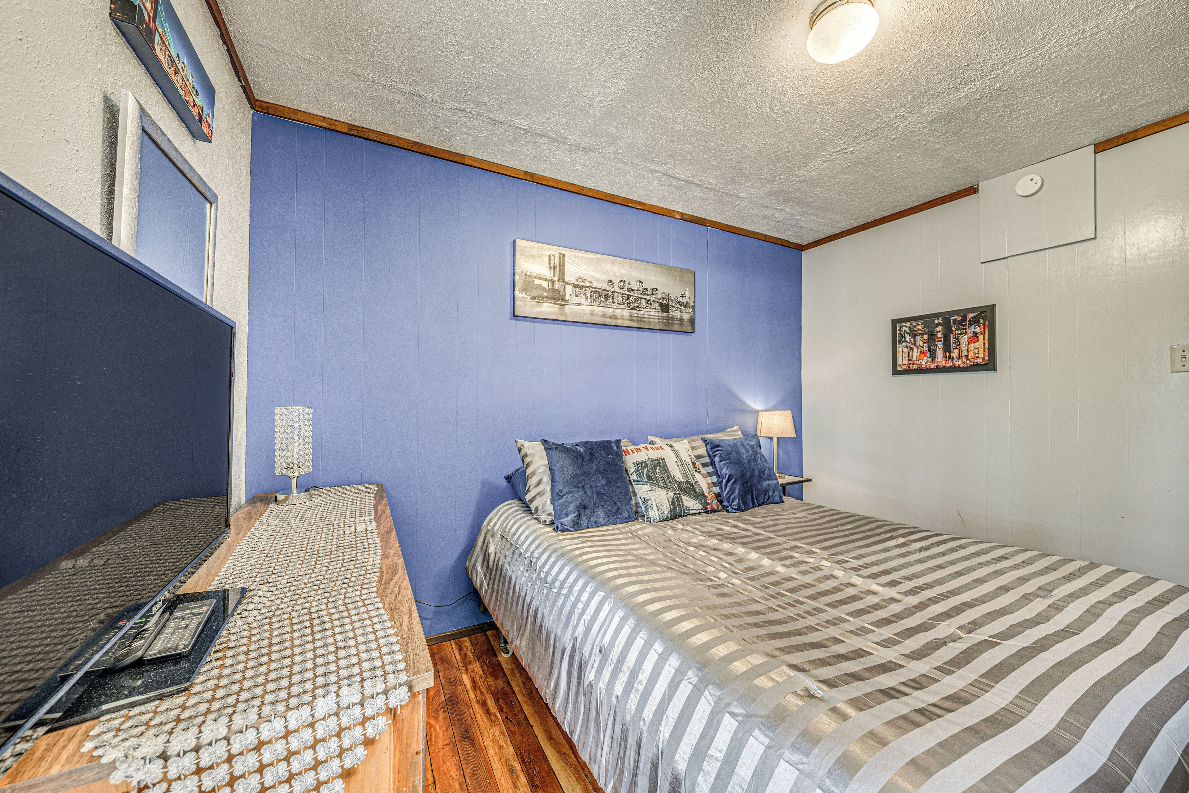 A bedroom with a bed, a desk, and a chair. There are two paintings on the wall.
