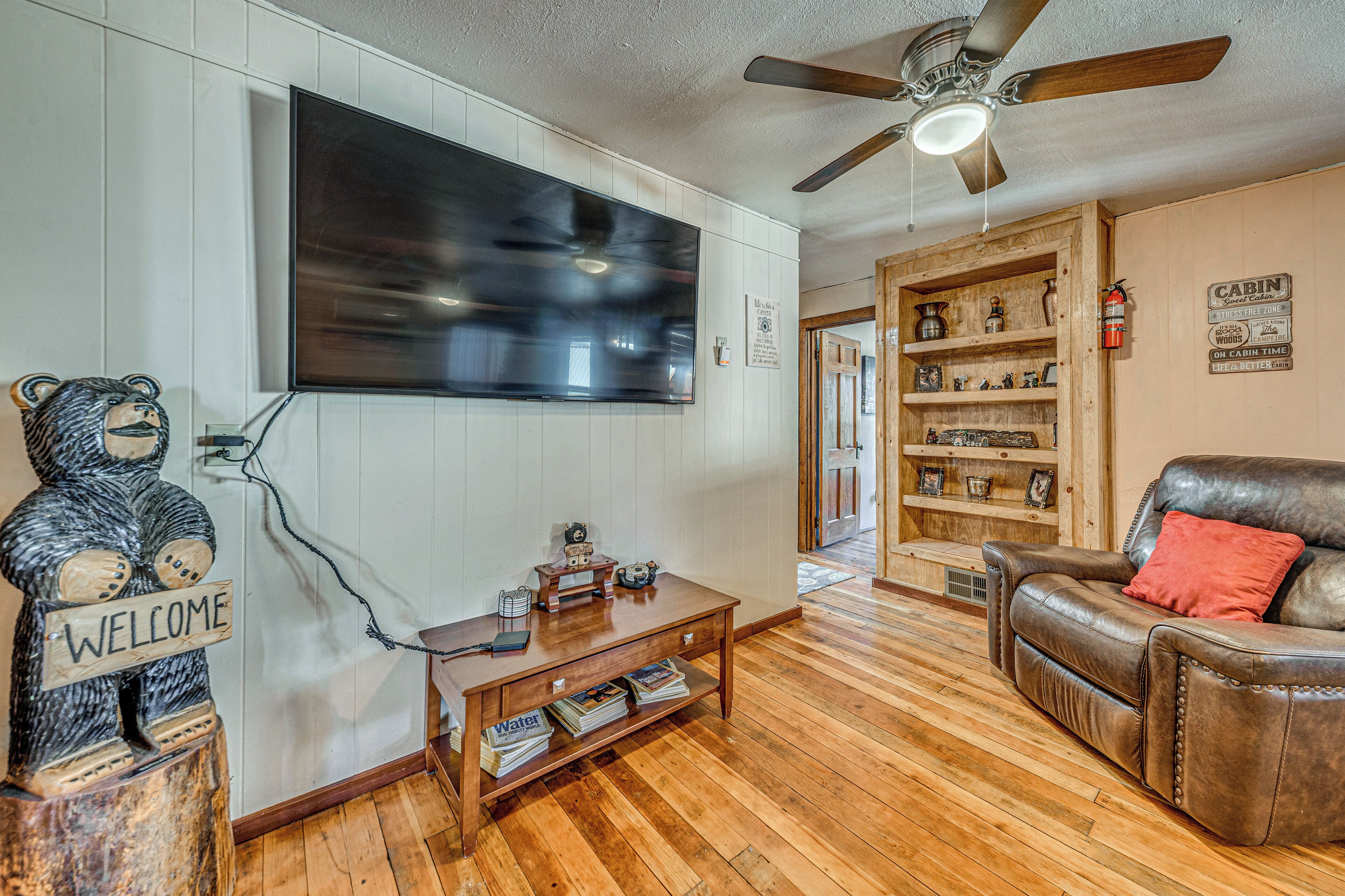 A living room with a mounted TV, wooden furniture, a bear sculpture, and a bookshelf.