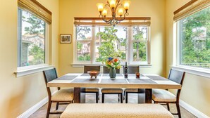 A dining room with a large table, chairs, a chandelier, and a window with a view of houses. - Steps to Bay: Tranquil Navarre Retreat w/ Balcony (Navarre)