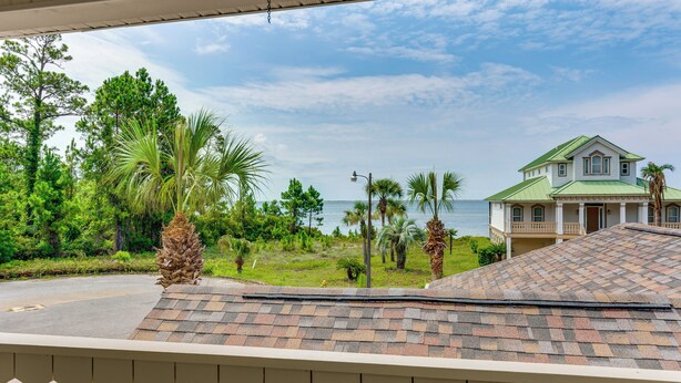 A house with a green roof, surrounded by lush greenery and a view of the ocean. - Steps to Bay: Tranquil Navarre Retreat w/ Balcony (Navarre)