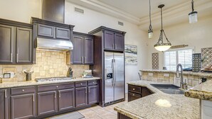 Une cuisine moderne avec des meubles de couleur sombre, des plans de travail en granit, des appareils électroménagers en acier inoxydable et des luminaires suspendus.