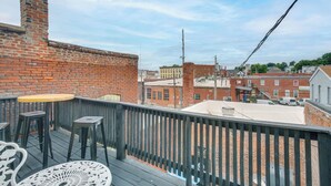 A rooftop terrace with a brick wall, a metal railing, and a table with chairs. - Deck + River View: Loft in Downtown Hannibal (Hannibal)