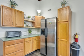 A kitchen with wooden cabinets, a stainless steel refrigerator, a microwave, and a trash bin. - Deck + River View: Loft in Downtown Hannibal (Hannibal)