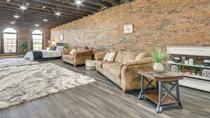 A spacious living room with a brick wall, wooden beams, and a large window. There are two sofas and a coffee table. - Deck + River View: Loft in Downtown Hannibal (Hannibal)