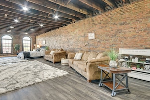 A spacious living room with a brick wall, wooden beams, and a large window. There are two sofas and a coffee table.