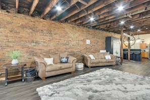 A rustic living room with exposed brick walls, wooden beams, and a cozy fireplace. There are two leather sofas with throw pillows and a fluffy rug. - Deck + River View: Loft in Downtown Hannibal (Hannibal)