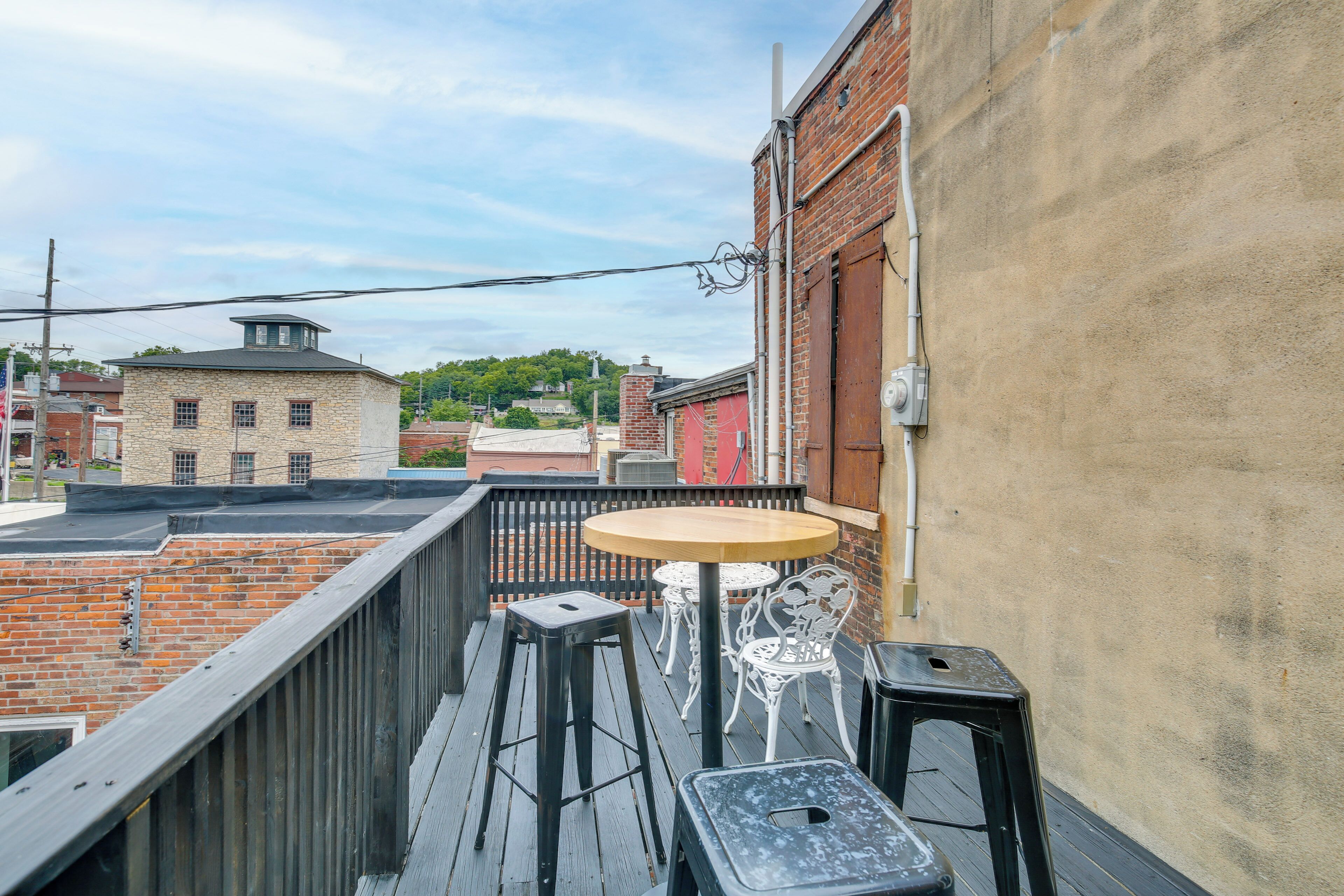 A balcony with a round table and two chairs, overlooking a cityscape with brick buildings.