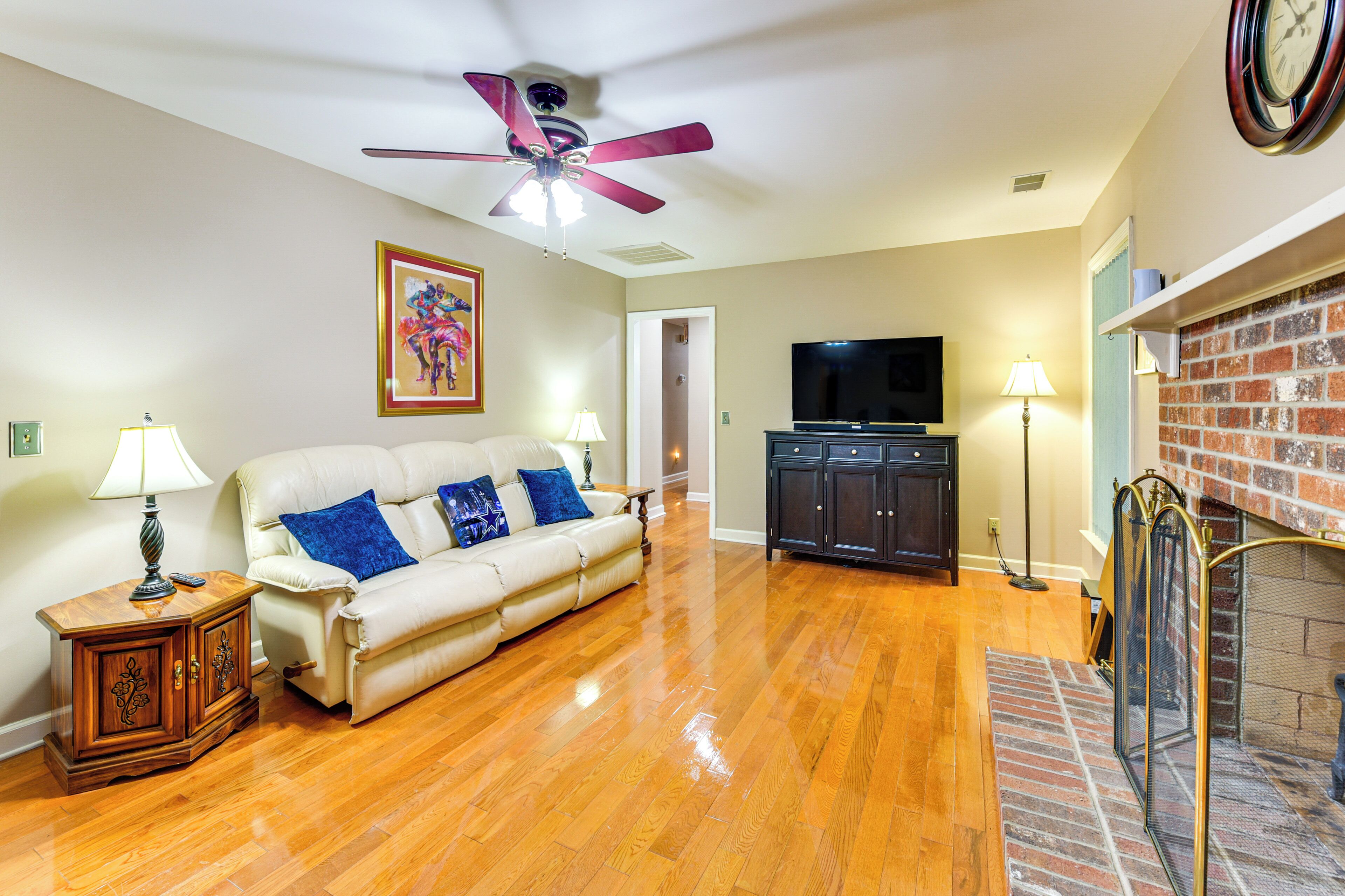A living room with a white sofa, a ceiling fan, a flat-screen TV, and a brick fireplace.