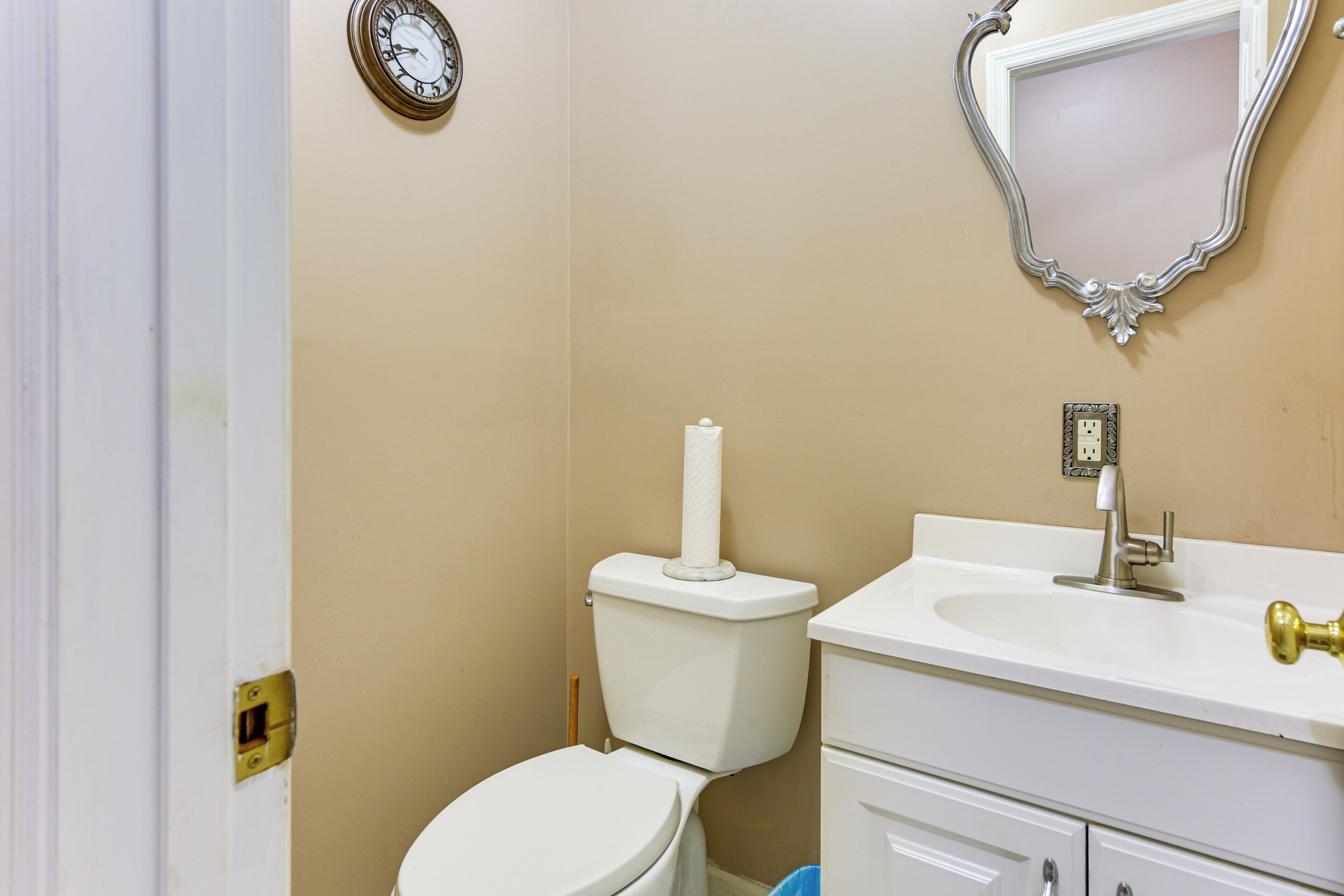 A bathroom with a toilet, sink, mirror, and clock.