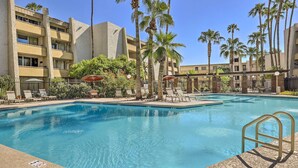 A swimming pool with lounge chairs and umbrellas, surrounded by palm trees and a multi-story building. - Walkable Old Town Scottsdale Condo: Pool & Hot Tub (Scottsdale)