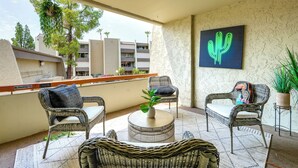 A balcony with wicker furniture, a cactus painting, and a view of buildings. - Walkable Old Town Scottsdale Condo: Pool & Hot Tub (Scottsdale)