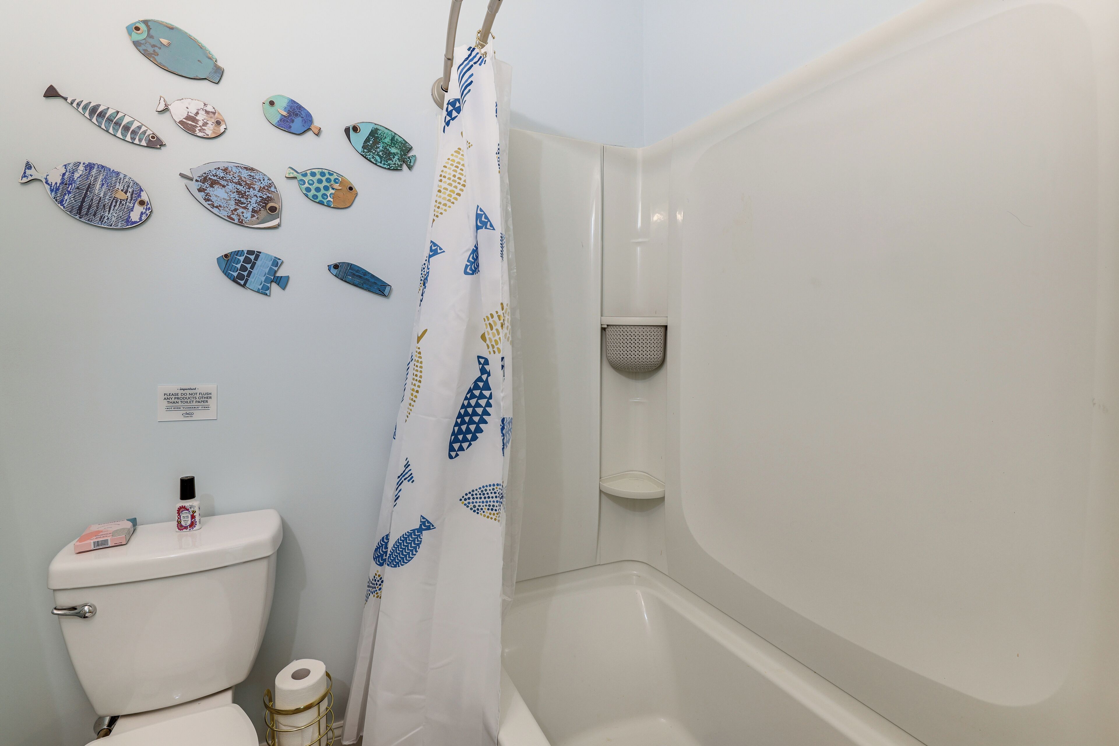 A bathroom with a toilet, a shower curtain with fish decals, and a toilet paper holder.