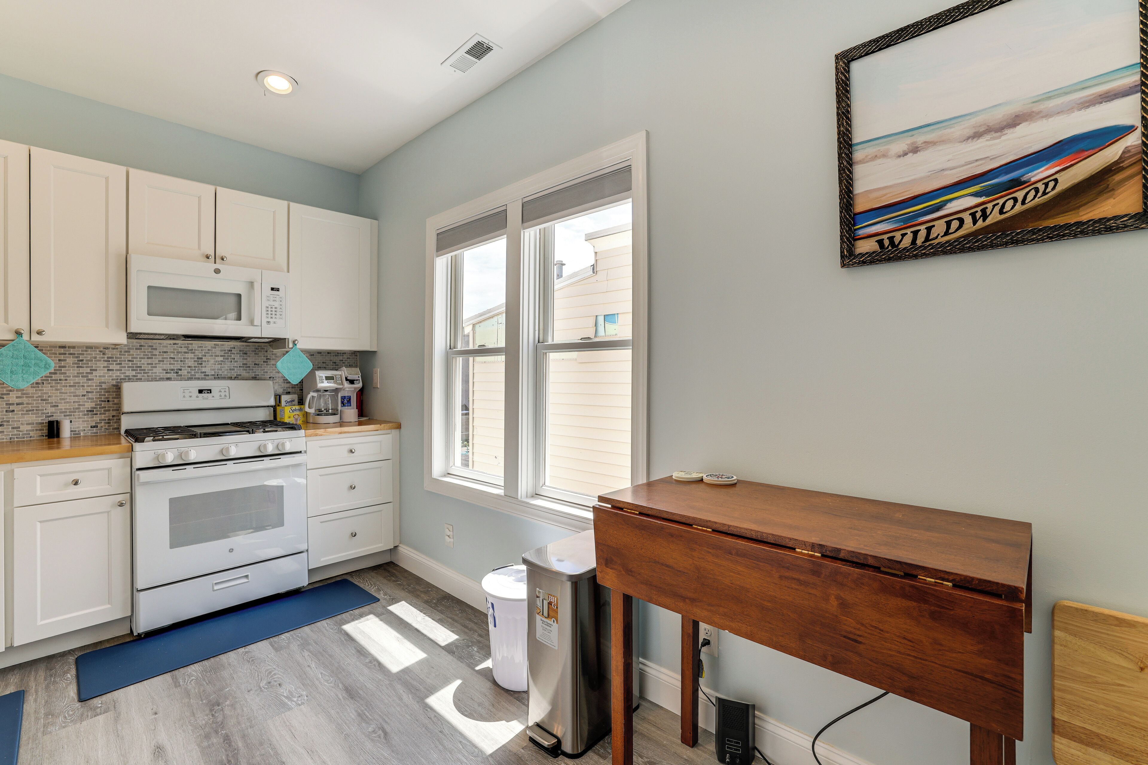 A kitchen with white cabinets, a microwave, an oven, a coffee maker, and a window with blinds.