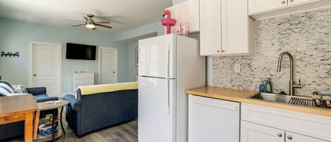 A compact living space with a kitchenette, a ceiling fan, a flat-screen TV, and a blue sofa.