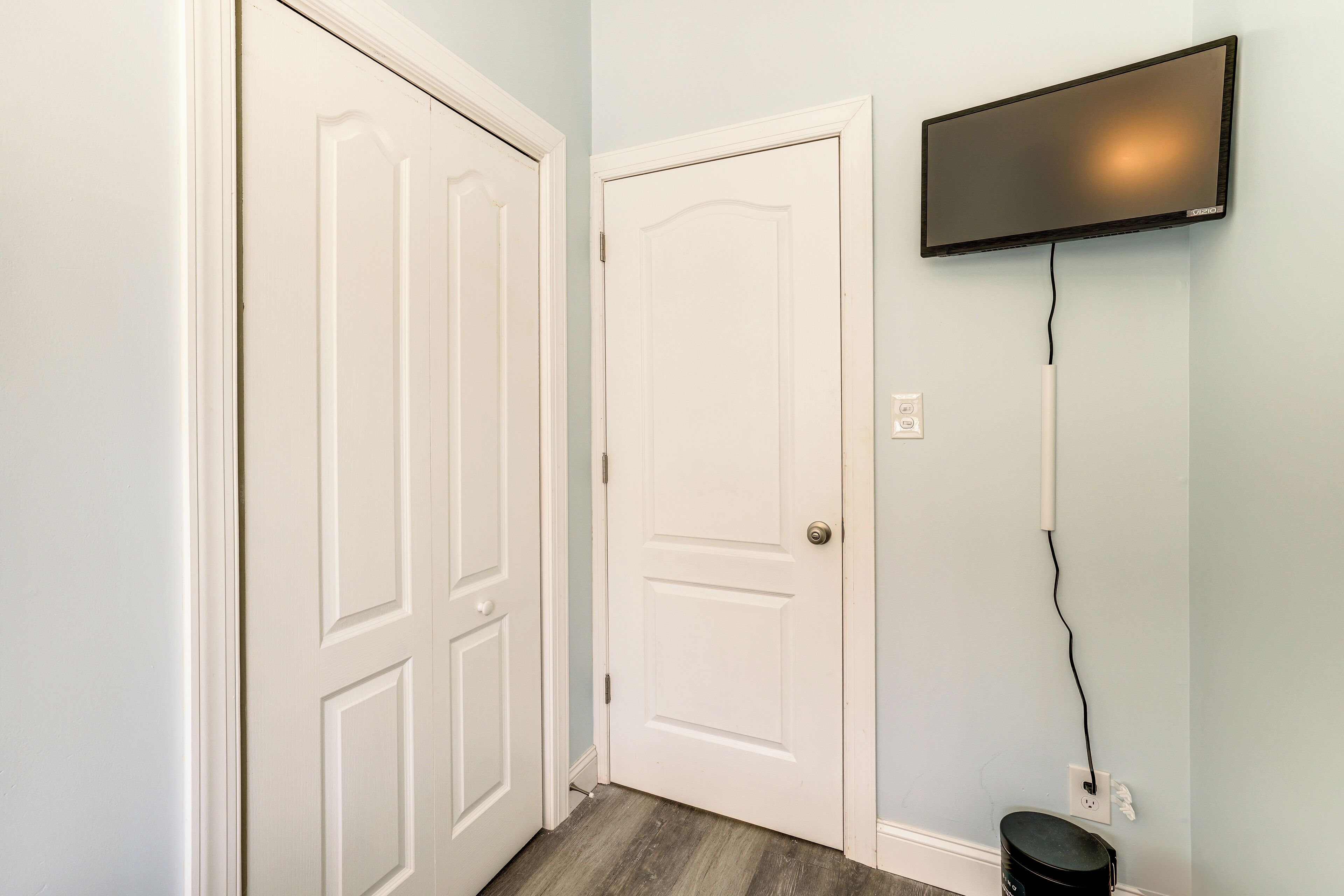 Un couloir avec deux portes blanches, un téléviseur à écran plat fixé au mur et une prise électrique sur le mur.