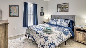 Quarto com uma cama grande, um ventilador de teto, um mapa na parede e uma mesa de cabeceira com uma luminária.
