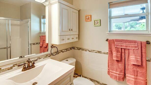 Une salle de bain avec un lavabo blanc, un miroir, des toilettes et une fenêtre donnant sur un paysage verdoyant.