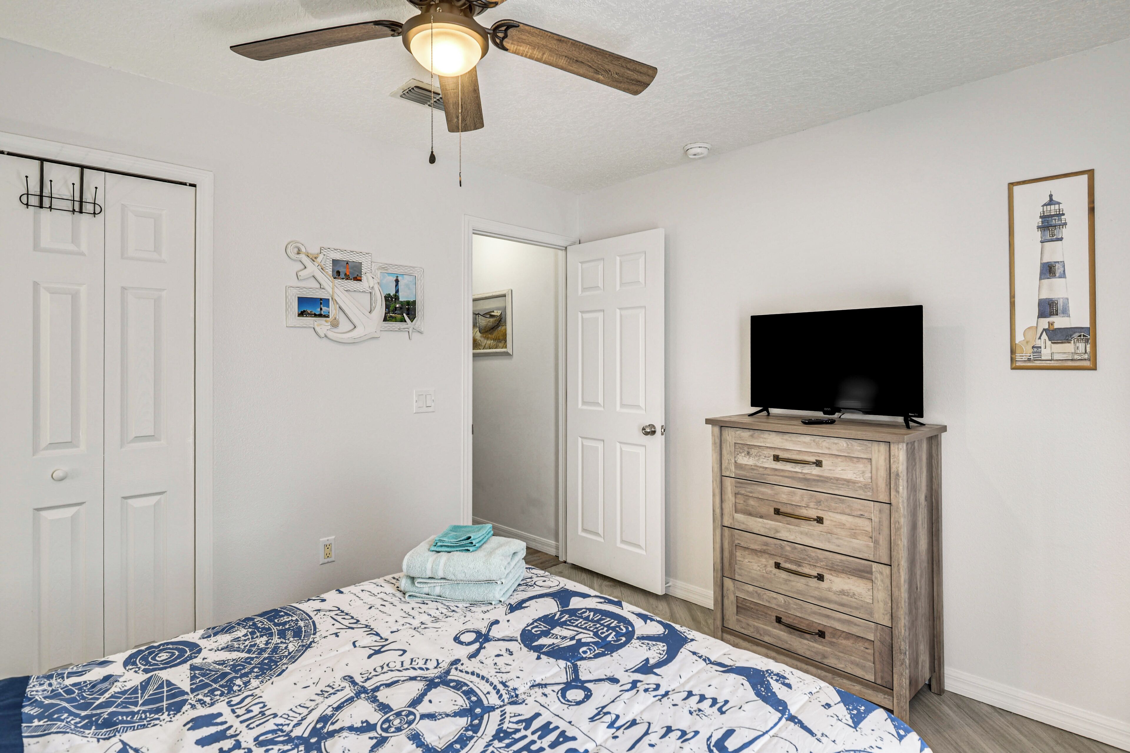 A bedroom with a bed, a ceiling fan, a dresser, a television, and a door leading to another room.